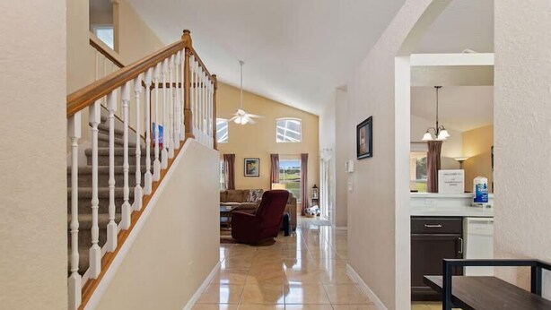 A hallway with a wooden staircase, a living room with a red armchair, and a kitchen area with a white countertop. - Highlands Reserve 4 Bed Pool Home with Spa - Golf Course Views (Davenport)