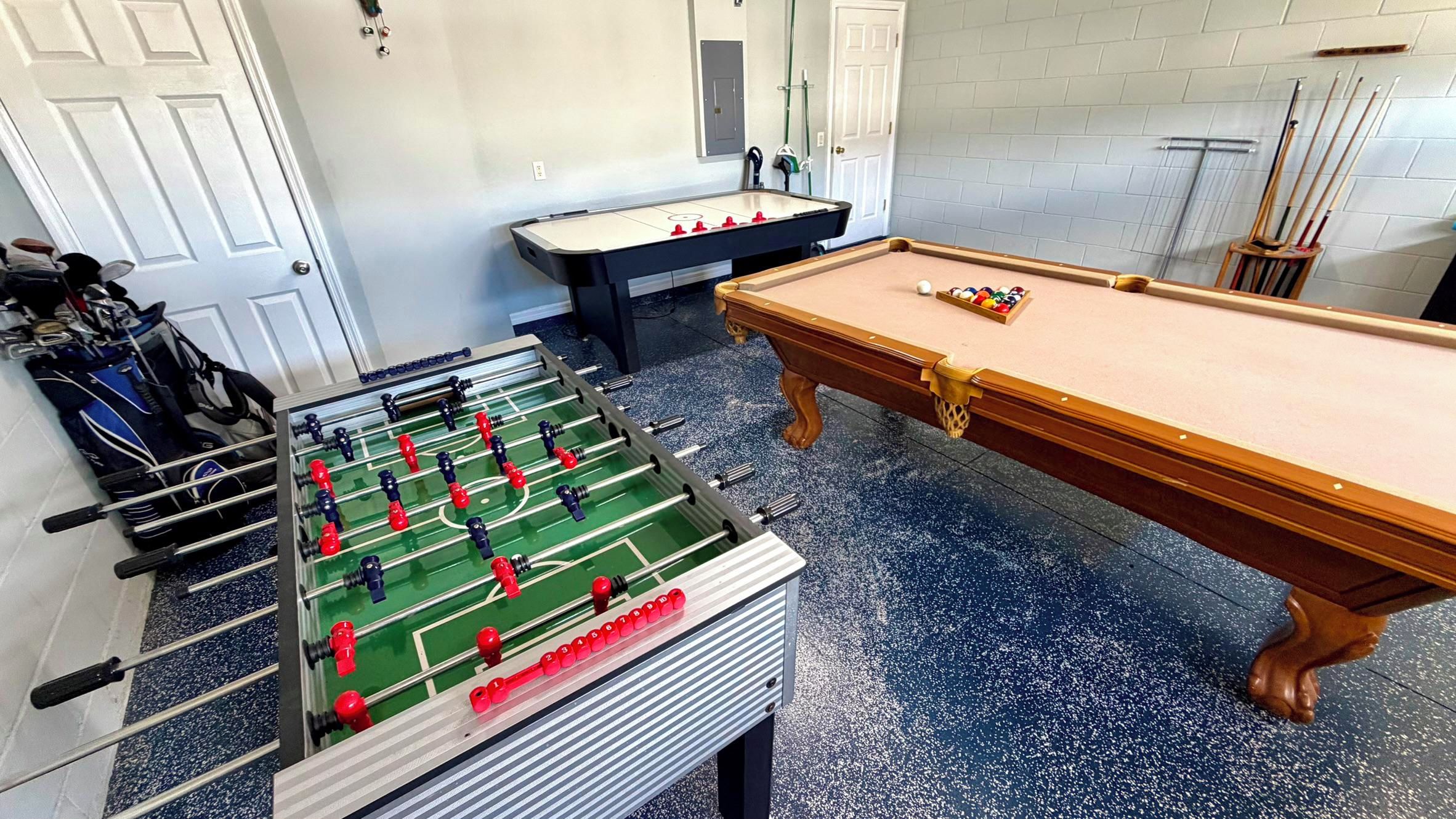 A room with a foosball table, a pool table, and a rack of golf clubs.