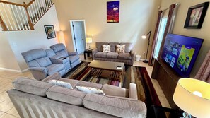 A living room with a grey sofa, a coffee table, a TV, and a staircase. - Highlands Reserve 4 Bed Pool Home with Spa - Golf Course Views (Davenport)