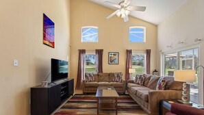 A living room with a large flat-screen TV, two sofas, a coffee table, and a ceiling fan. - Highlands Reserve 4 Bed Pool Home with Spa - Golf Course Views (Davenport)