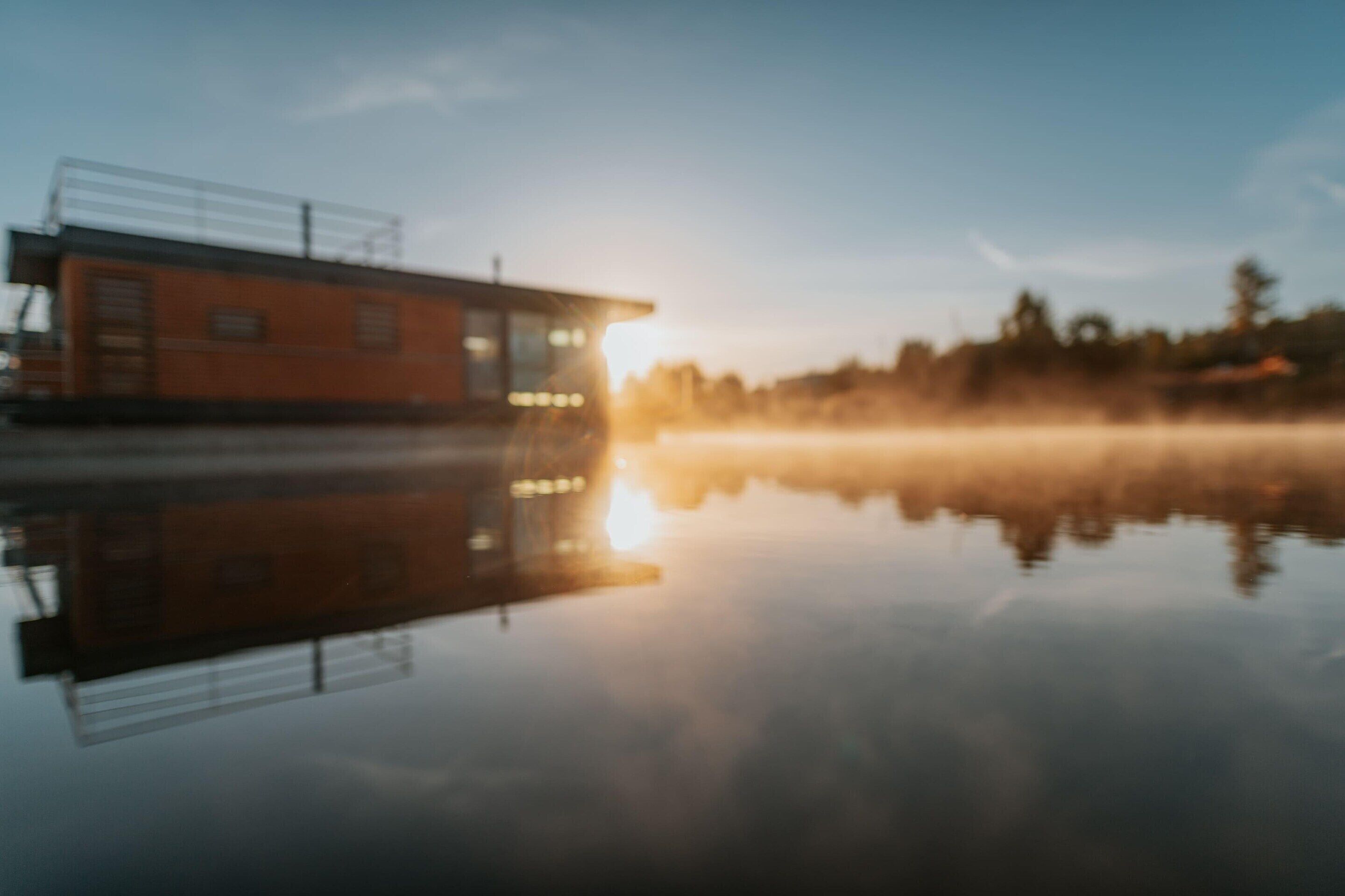A building with a flat roof and a large window, reflecting on a calm body of water.