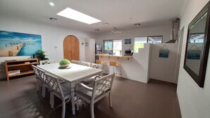 A dining area with a wooden table and chairs, a potted plant, and a painting of a pier. - SandNSea - Only Steps to the beach -Pet Friendly Accommodation (Burrum Heads)