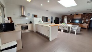A modern kitchen with white cabinetry, a built-in oven, and a dining area with a white table and chairs. - SandNSea - Only Steps to the beach -Pet Friendly Accommodation (Burrum Heads)