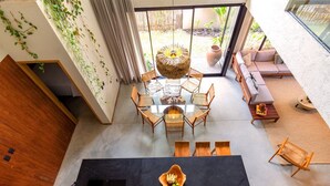 A modern interior with a glass dining table surrounded by wicker chairs, a black countertop with a fruit bowl, and a cozy seating area with cushions and a sofa. - Casa Alma - By Living Milagres (Passo de Camaragibe)