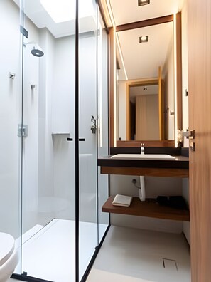 A modern bathroom with a glass shower enclosure, a wooden vanity with a mirror, and a white toilet. - Casa Alma - By Living Milagres (Passo de Camaragibe)