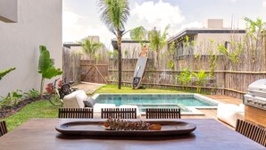A poolside view with a dining table, chairs, and a grill. - Casa Alma - By Living Milagres (Passo de Camaragibe)
