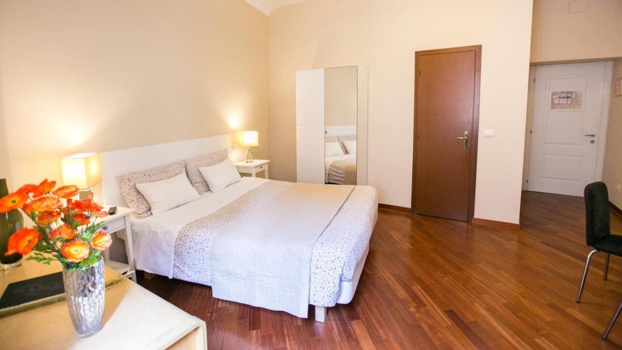 A neatly arranged bedroom with a bed, bedside tables, a mirror, a door, and a chair.