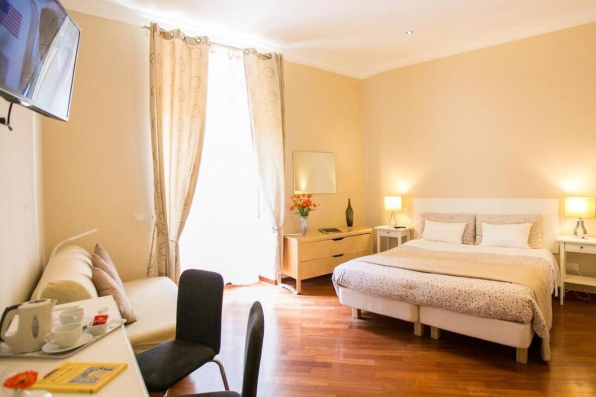 Une chambre d’hôtel comprenant un lit, des tables de chevet, un bureau avec une chaise, une télévision et une fenêtre avec des rideaux.