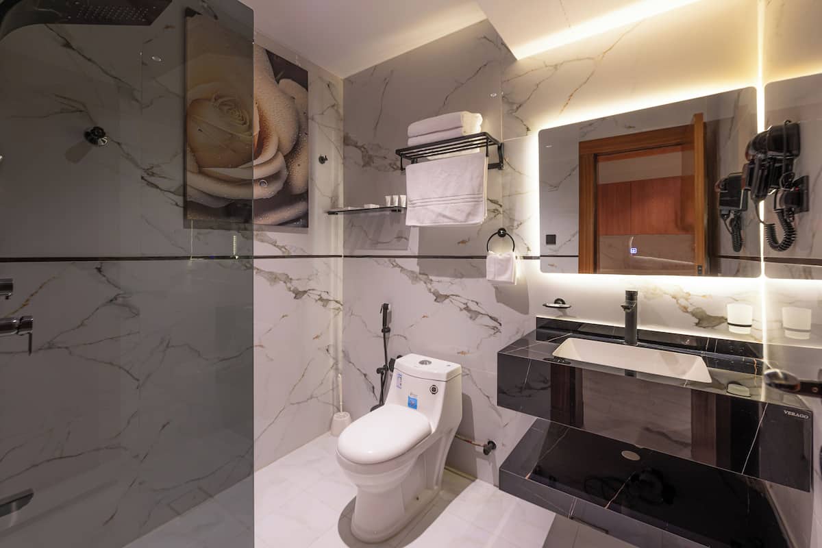 A modern bathroom with a marble wall, a toilet, a glass shower enclosure, a sink with a mirror, and a towel rack.
