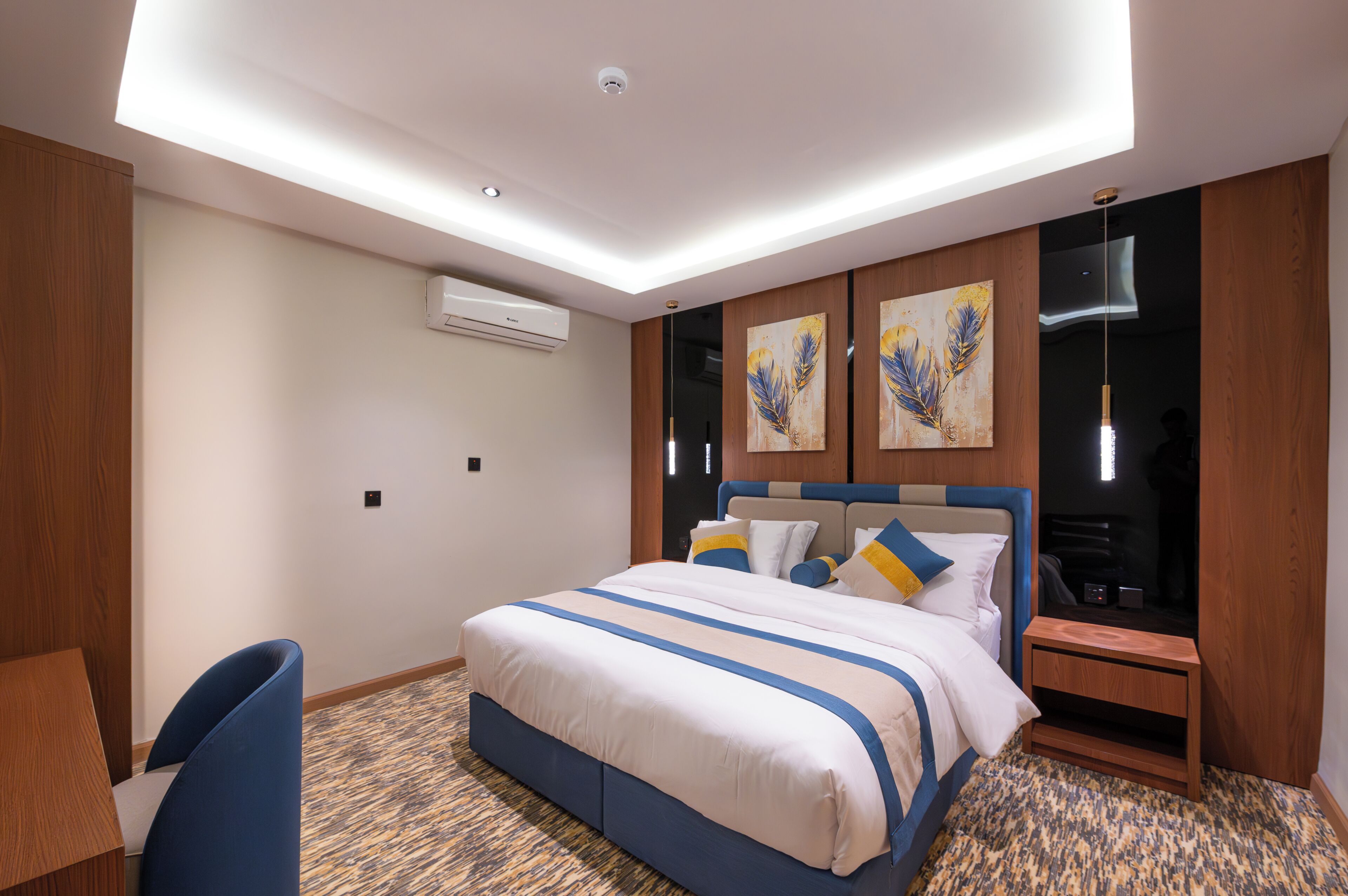 A hotel room with a bed, a desk, a chair, a nightstand, and artwork on the wall.