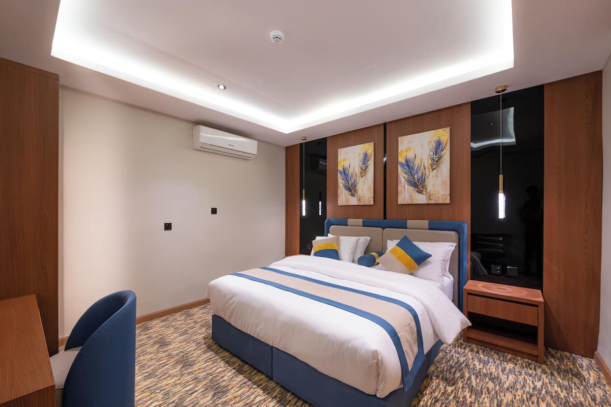 A hotel room with a bed, a desk, a chair, a nightstand, and artwork on the wall.