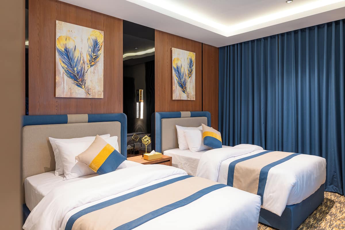 A hotel room with two beds, wooden paneling, artwork on the walls, and a large window with curtains.