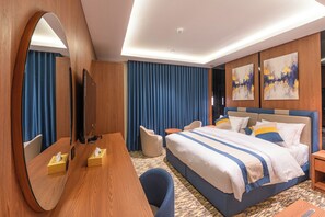 A hotel room with a large bed, a desk, a chair, a mirror, and two paintings on the wall. - MEDAD ALSHATEA SERVICED APARTMENTS (Dammam)
