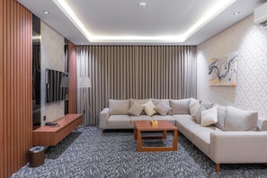 A modern living room with a sofa, a coffee table, a TV, and a painting on the wall. - MEDAD ALSHATEA SERVICED APARTMENTS (Dammam)