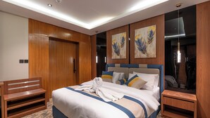 Ein Hotelzimmer mit einem großen Bett, einem Holz-Kopfteil, einer Bank, einem kleinen Tisch und Bildern an den Wänden.