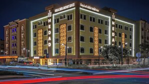 Ein mehrstöckiges Hotel mit beleuchteter Beschilderung, einem Parkplatzschild und Blick auf die Straße mit Lichtspuren.