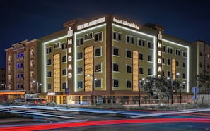 A multi-story hotel with illuminated signage, a parking sign, and a view of the street with light trails. - MEDAD ALSHATEA SERVICED APARTMENTS (Dammam)
