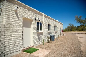 A white stone building with a door, windows, and a small garden area.