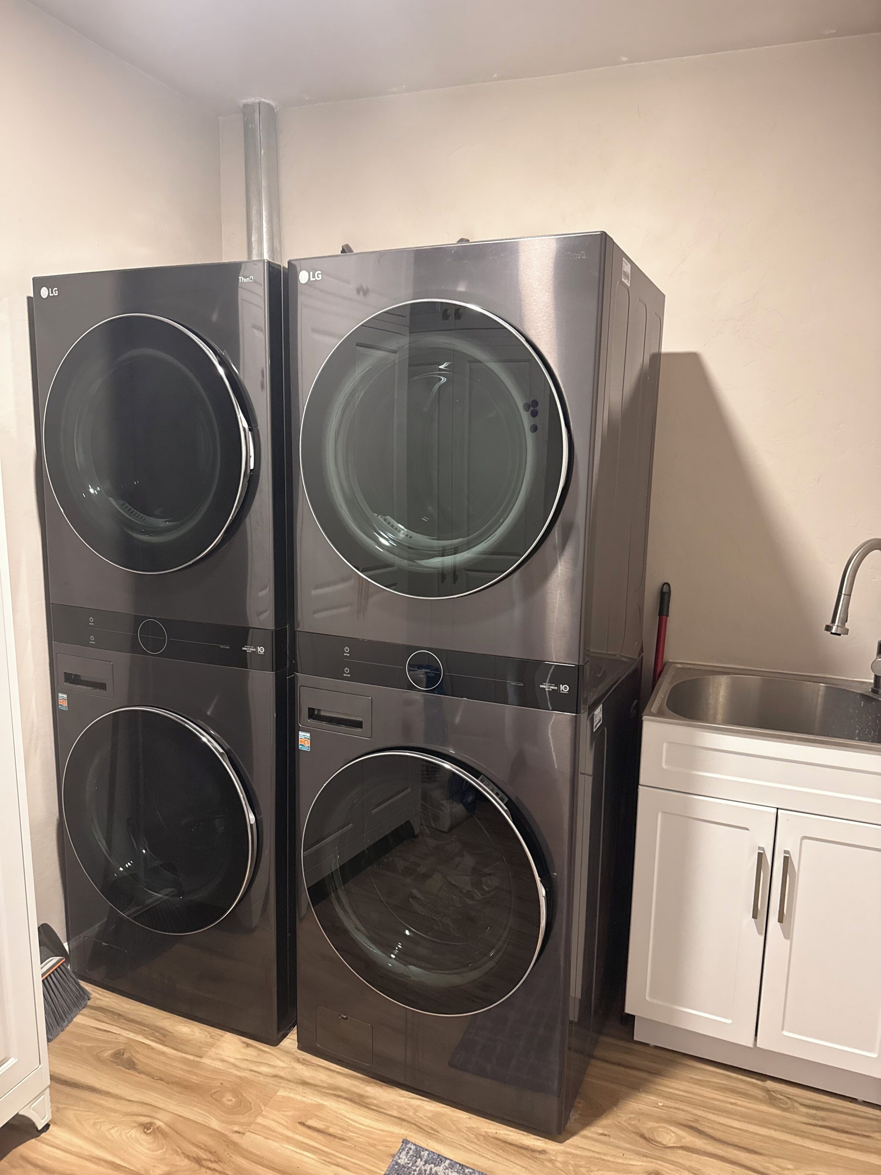 A laundry room with two stacked front-loading washers and a sink.