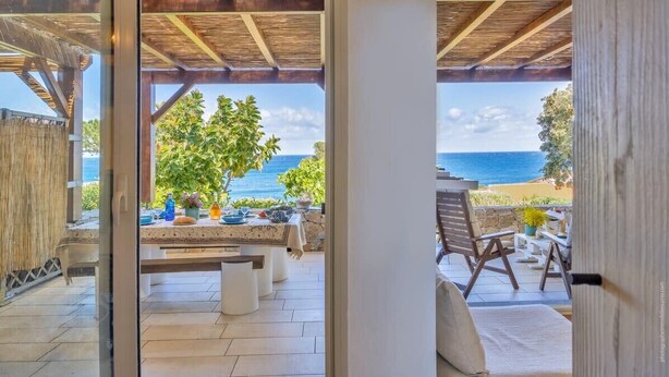A covered outdoor area with a view of the sea, a dining table with chairs, and a wooden pergola. - Casa Libecciu (Lumio)