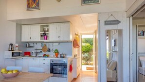 A compact kitchen with white cabinets, a microwave, a toaster, and a sink. There is a dining table with chairs and a bowl of fruit. A sign indicates a tour of the property. - Casa Libecciu (Lumio)