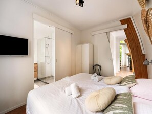 Una camera da letto con un letto, cuscini, una TV, un armadio e un box doccia.