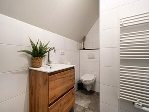 Un bagno con piastrelle bianche, un mobile bagno in legno, un lavandino, un water e un termosifone.