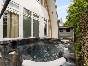 Area con vasca idromassaggio, un patio in legno, un edificio bianco con ampie finestre e un piccolo deposito sullo sfondo.