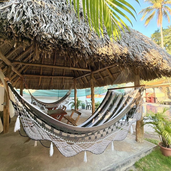 A hammock under a thatched roof structure, wooden furniture, and a palm tree.