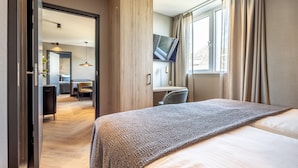A hotel room with a bed, a desk, a chair, a TV, and a window with curtains.