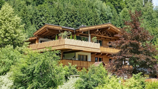 A wooden chalet with a balcony, surrounded by dense forest. - Apartments Niederseer - Reiterkogel (Saalbach)