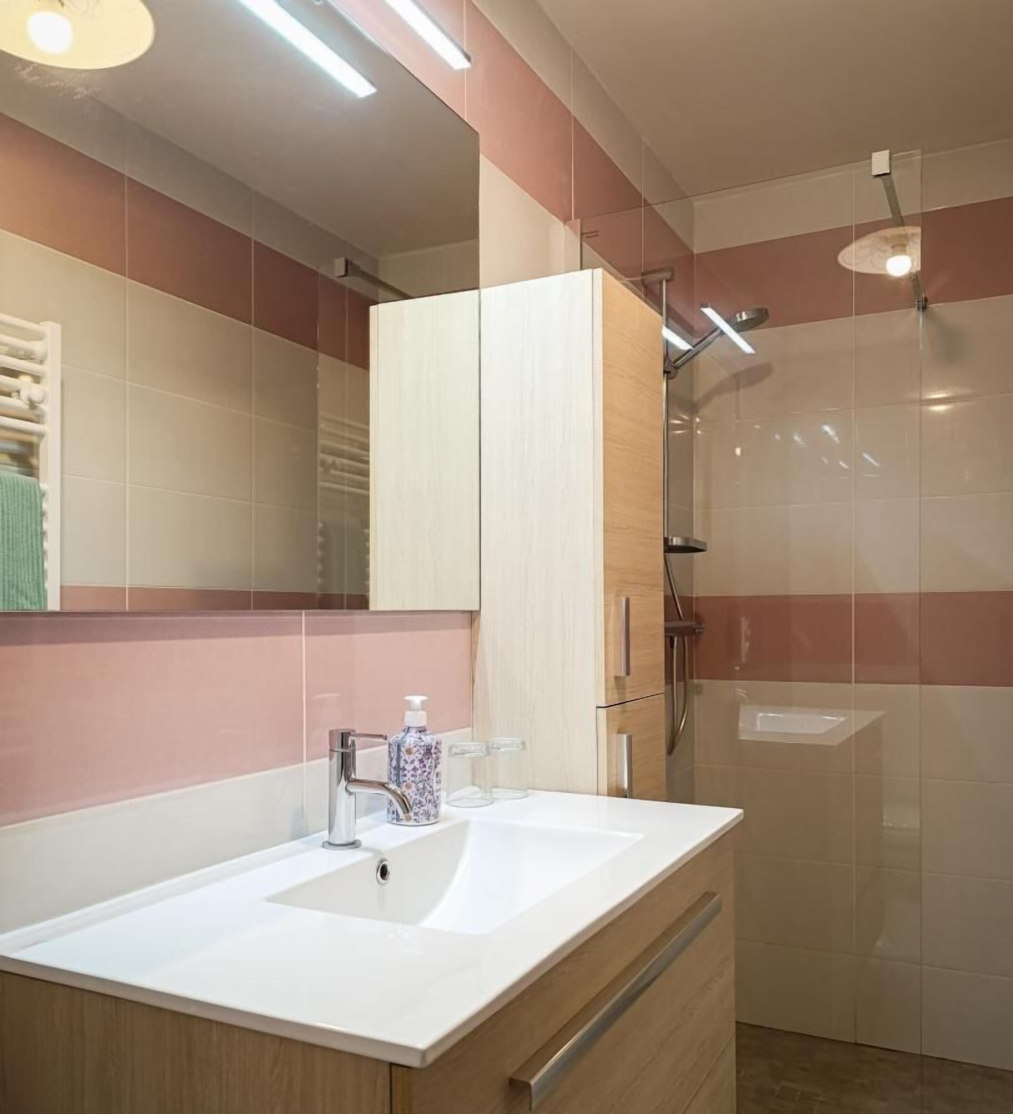 A modern bathroom with a white sink, a mirror, and a shower area.