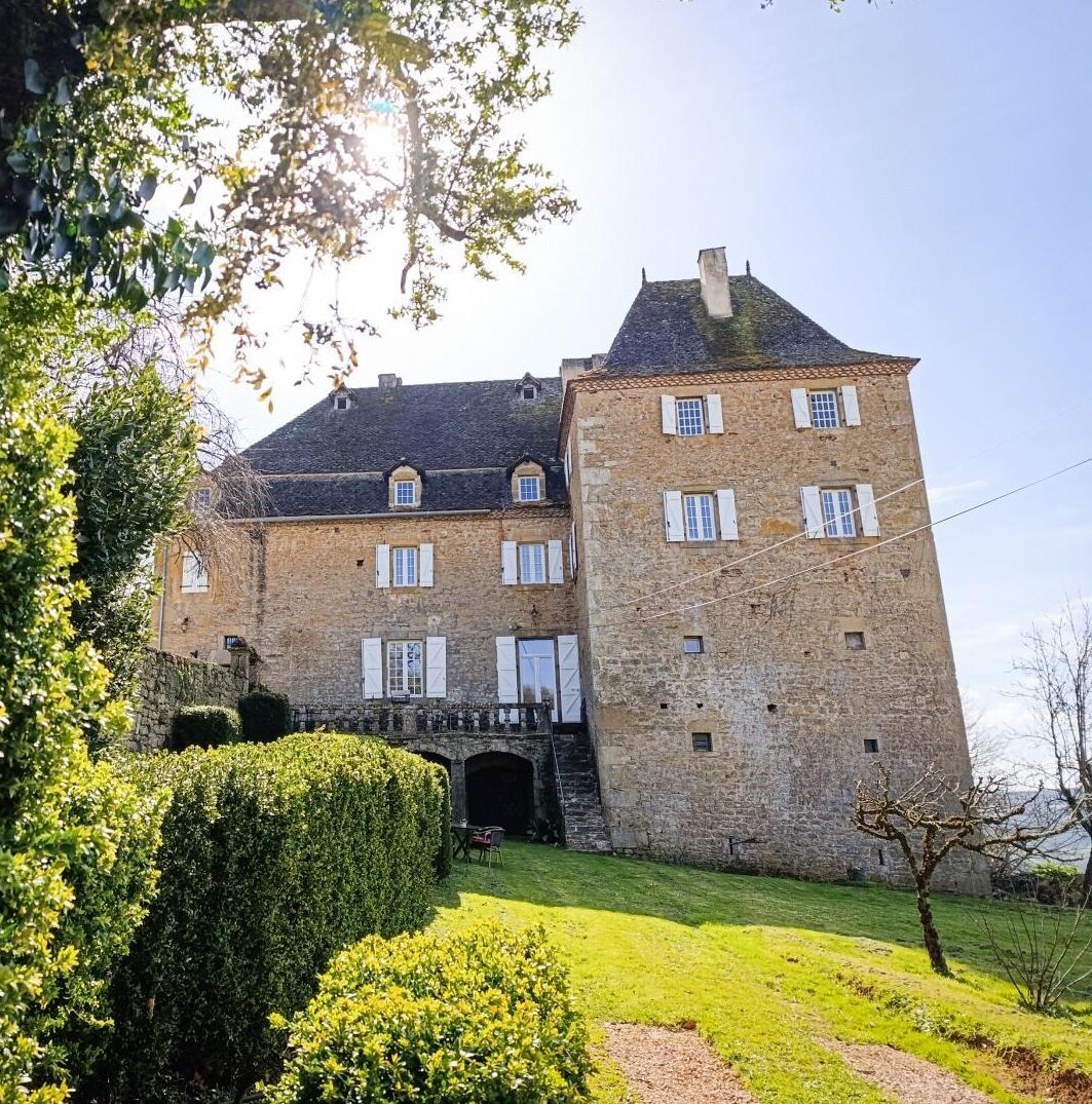 A historic stone building with a prominent tower, a central entrance, and a well-maintained garden.