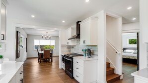 A modern kitchen with white cabinetry, a black stove, and a dining area with a wooden table and chairs. - Entertainment Haven / Pool Table (Portland)