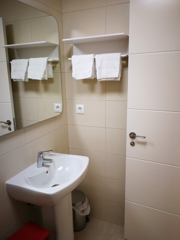 A bathroom with a white sink, a mirror, a red stool, and a trash can.