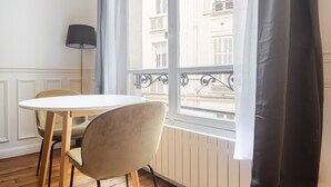 A room with a round table and two chairs, a floor lamp, and a window with a view of buildings.