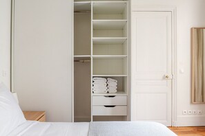 Een slaapkamer met een bed, een nachtkastje, een witte kledingkast met planken en een deur.