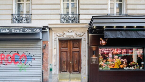 A storefront with a closed metal shutter, a wooden double door, and a display window with various products.