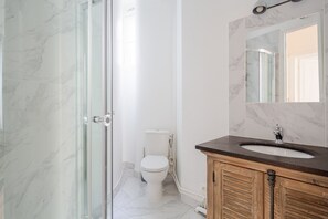 Een badkamer met een glazen douchedeur, toilet en een wastafel met een marmeren aanrechtblad.