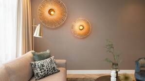 En moderne stue med en beige sofa, mønstrede puder, en gulvlampe og dekorative væglamper.