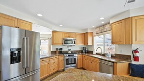 A modern kitchen with stainless steel appliances, wooden cabinets, granite countertops, and a built-in microwave. - Beach Perfection | Private Spa, Rooftop Views, Outdoor Kitchen & Garage Parking (San Diego)