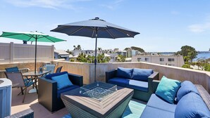 A rooftop terrace with outdoor furniture, including sofas and a table, and two umbrellas providing shade. - Beach Perfection | Private Spa, Rooftop Views, Outdoor Kitchen & Garage Parking (San Diego)