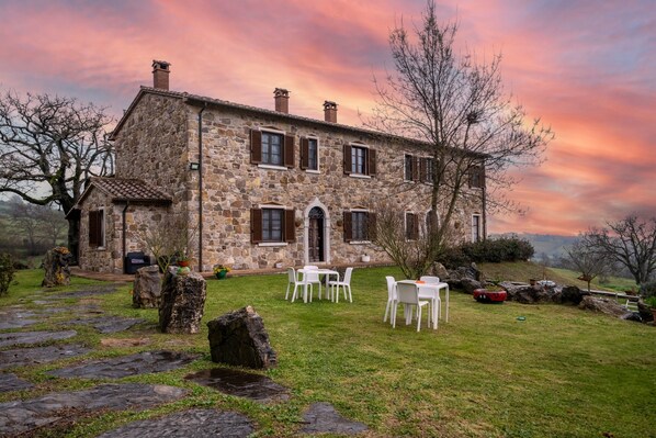 A stone building with a stone pathway leading to a white table and chairs set outdoors.