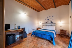 A bedroom with a bed, a desk, a television, and a small refrigerator. - Room 'Blu' with Shared Pool and Shared Garden (Semproniano)