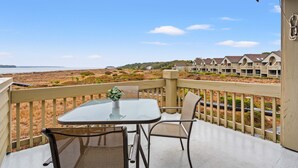 A balcony with a table and chairs overlooking a beach and a row of houses. - Beachfront w/ Breathtaking Views! 1BR/2BA, Pet Friendly, Amenity Access included (Seabrook Island)