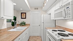 A modern kitchen with white cabinets, a double sink, a stove, and a microwave. - Beachfront w/ Breathtaking Views! 1BR/2BA, Pet Friendly, Amenity Access included (Seabrook Island)
