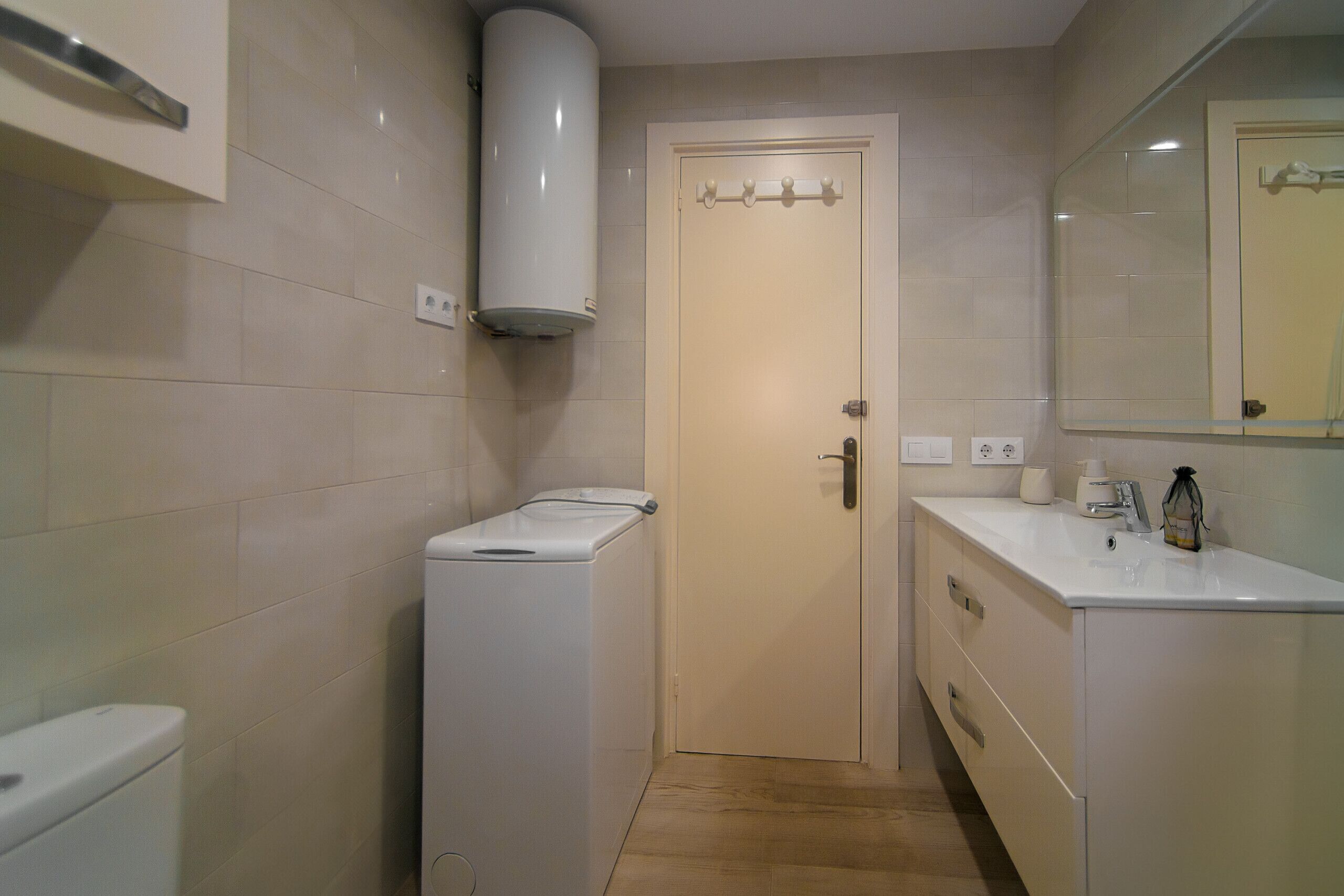A compact bathroom with a toilet, a washing machine, and a sink with a mirror above it.