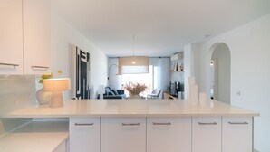 A modern kitchen with white cabinetry, a central island, and a dining area with a sofa and chairs. - WELCS APARTAMENTO 223 EMP con TERRAZA con VISTA (Empuriabrava)
