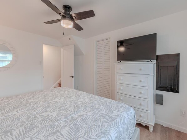 A bedroom with a bed, a dresser, a television, and a ceiling fan.