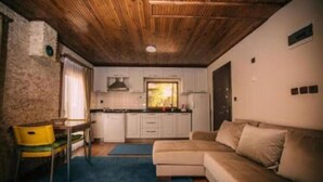 A compact living space with a wooden ceiling, a kitchenette, a beige sofa, and a yellow chair. - Ak Nature  (Trabzon)